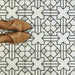Azulejos de estilo marroquí Alhambra Palacio 20x20 cm con patrón geométrico en cruz en negro sobre base blanca, mostrados desde arriba junto a zapatos en tono camel para destacar el diseño detallado y el acabado mate.