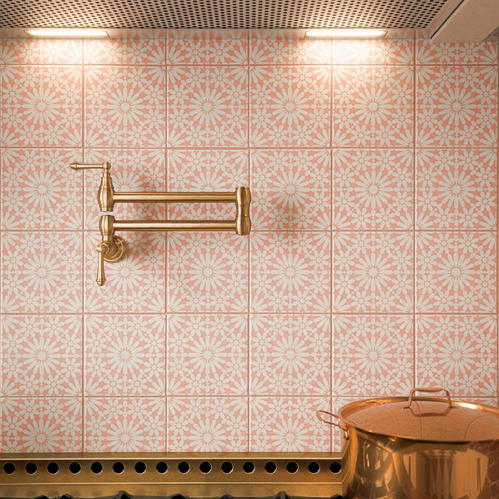 Primer plano de los azulejos de pared Fizaan Pink de 20 × 20 cm de estilo marroquí, con delicados motivos florales en forma de estrella en tonos rosa y crema, creando un salpicadero decorativo en la cocina, acompañado de grifería en acabado latón y utensilios de cocina de cobre.