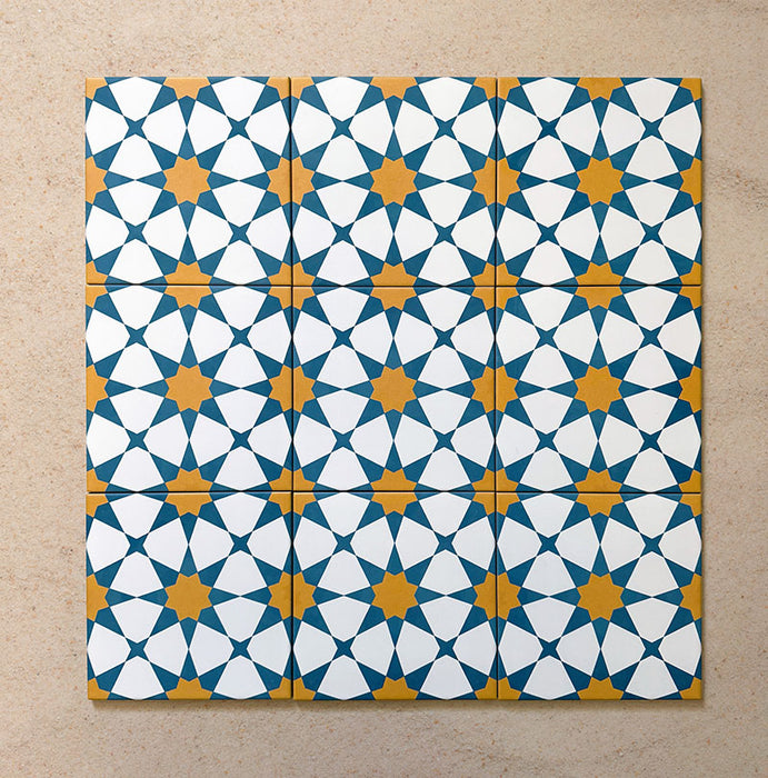 Primer plano de varios azulejos cerámicos de estilo marroquí Agraba Sunshine 20x20 cm colocados en cuadrícula, mostrando un vibrante patrón geométrico de estrellas en azul, amarillo mostaza y blanco sobre fondo arena neutro.