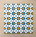 Primer plano de varios azulejos cerámicos de estilo marroquí Agraba Sunshine 20x20 cm colocados en cuadrícula, mostrando un vibrante patrón geométrico de estrellas en azul, amarillo mostaza y blanco sobre fondo arena neutro.
