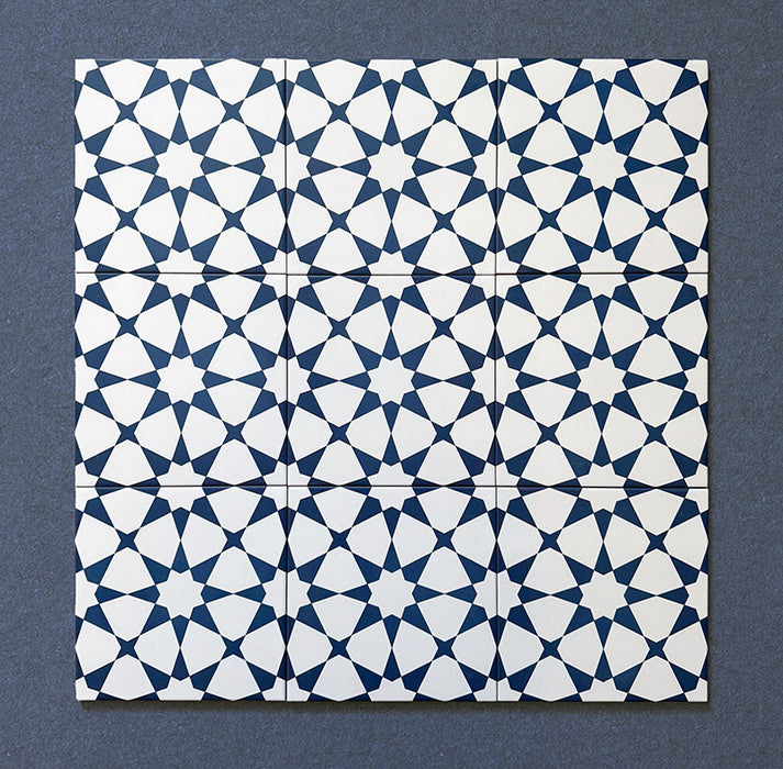 Primer plano de varios azulejos cerámicos de estilo marroquí Agraba Azul Marino 20x20 cm colocados en cuadrícula, mostrando un patrón geométrico de estrellas repetido en azul marino y blanco sobre fondo oscuro.