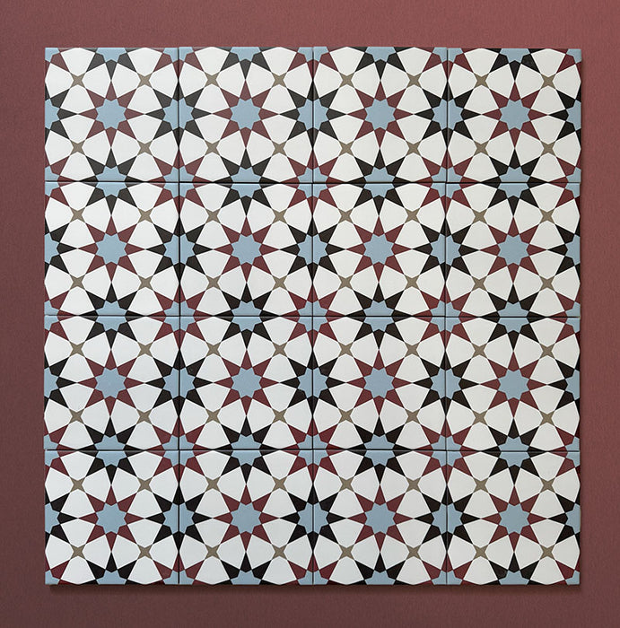 Primer plano de varios azulejos cerámicos de estilo marroquí Agraba Mini Atlas 15x15 cm colocados en cuadrícula, mostrando un colorido patrón geométrico de estrellas en azul, terracota, negro y blanco sobre fondo burdeos cálido.