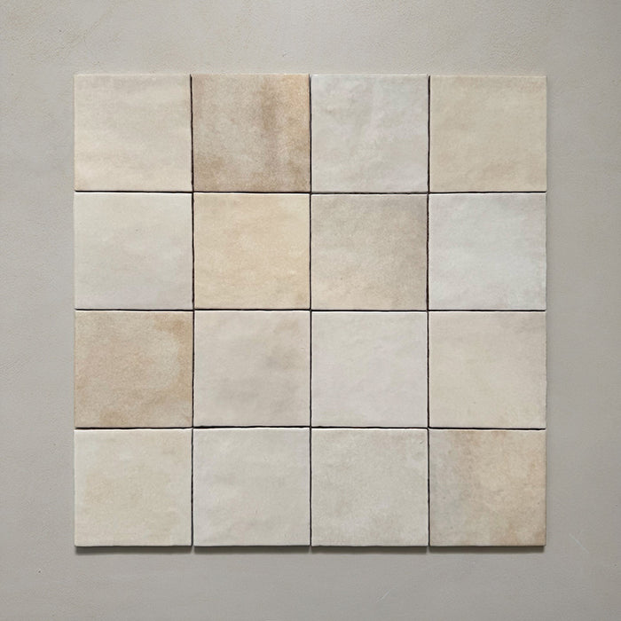 Vista cenital de azulejos de pared cerámicos Zellij Ocre Cuadrado 13,2 × 13,2 cm de estilo marroquí, dispuestos en cuadrícula, mostrando una suave variación tonal, bordes ligeramente irregulares y un acabado brillante con efecto artesanal en tonos neutros cálidos sobre un fondo liso.