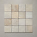 Vista cenital de azulejos de pared cerámicos Zellij Ocre Cuadrado 13,2 × 13,2 cm de estilo marroquí, dispuestos en cuadrícula, mostrando una suave variación tonal, bordes ligeramente irregulares y un acabado brillante con efecto artesanal en tonos neutros cálidos sobre un fondo liso.