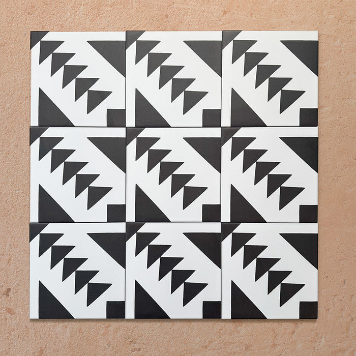 Disposición agrupada de azulejos de estilo marroquí Alhambra Alkazar 20x20 cm, mostrando un audaz patrón geométrico triangular en blanco y negro sobre fondo terracota cálido.