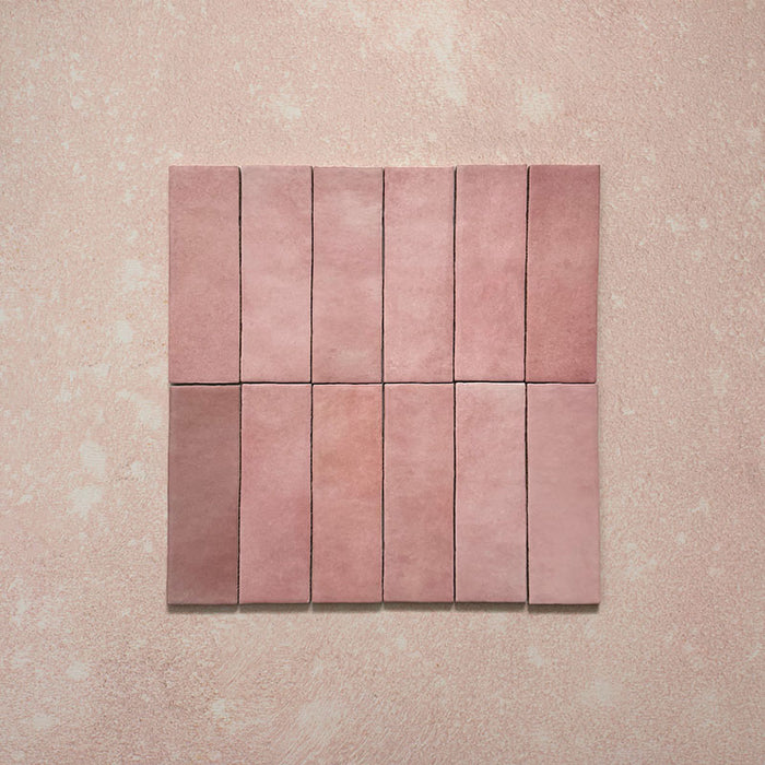 Vista cenital de azulejos de pared cerámicos Zellij Rosa Ladrillo 6,5 × 20 cm de estilo marroquí, dispuestos en cuadrícula, mostrando una suave variación tonal, bordes ligeramente irregulares y un acabado brillante con efecto artesanal en tonos rosados sobre un fondo texturizado.