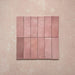 Vista cenital de azulejos de pared cerámicos Zellij Rosa Ladrillo 6,5 × 20 cm de estilo marroquí, dispuestos en cuadrícula, mostrando una suave variación tonal, bordes ligeramente irregulares y un acabado brillante con efecto artesanal en tonos rosados sobre un fondo texturizado.
