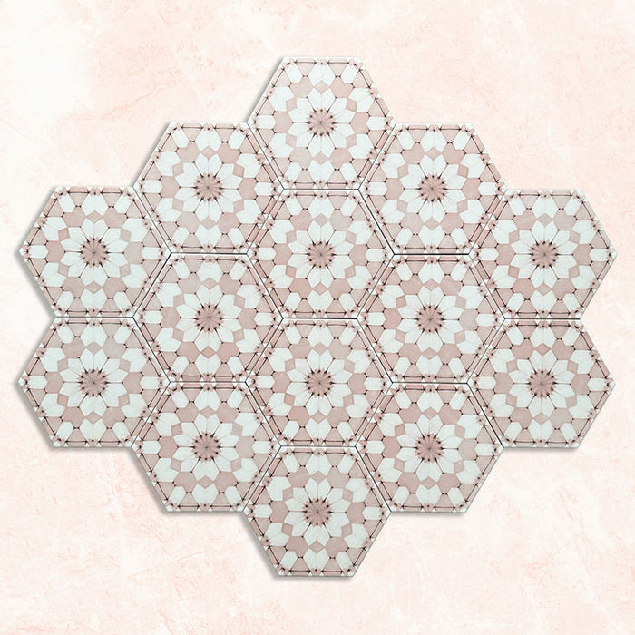 Baldosas hexagonales Maroush Rosa Empolvado 18,7x21,6 cm de estilo marroquí dispuestas en grupo, destacando el patrón floral en forma de estrella en rosa suave y blanco sobre un fondo efecto mármol claro.