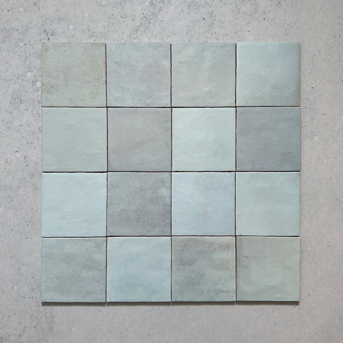 Vista cenital de azulejos de pared cerámicos Zellij Aqua Cuadrado 13,2 × 13,2 cm de estilo marroquí, dispuestos en cuadrícula, destacando la suave variación tonal en azul, el acabado brillante de aspecto artesanal y los bordes ligeramente irregulares.