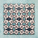Group image showing multiple Geometry Iris 20x20cm patterned tiles arranged in a repeating layout, featuring an intricate geometric design in teal, navy, terracotta-red, and cream, photographed against a soft mottled aqua background.