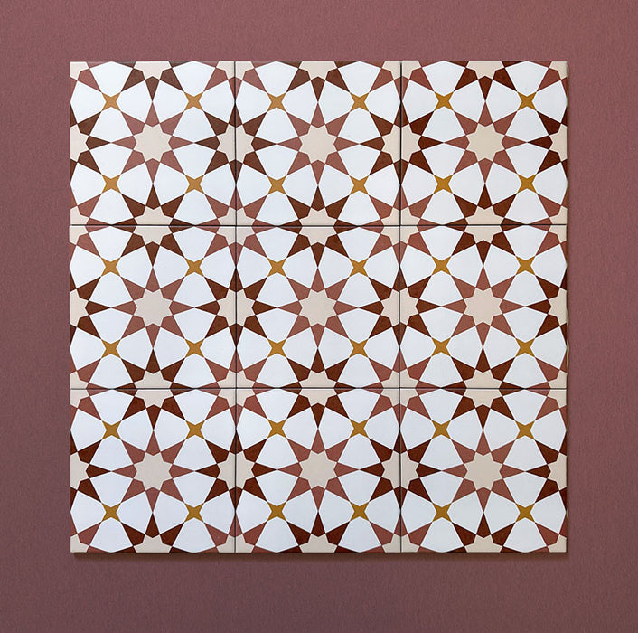 Primer plano de varios azulejos cerámicos de estilo marroquí Agraba Cotto 20x20 cm colocados en cuadrícula, mostrando un patrón geométrico de estrellas en terracota, beige, mostaza y blanco sobre fondo burdeos cálido.