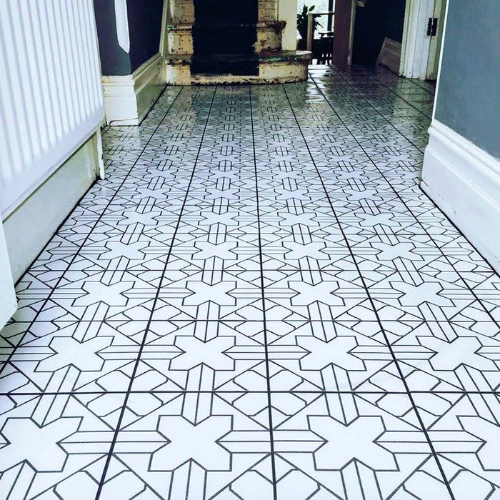 Azulejos de estilo marroquí Alhambra Palacio 20x20 cm utilizados en un pasillo, con detallado patrón geométrico en cruz en negro sobre fondo blanco para un suelo protagonista refinado.