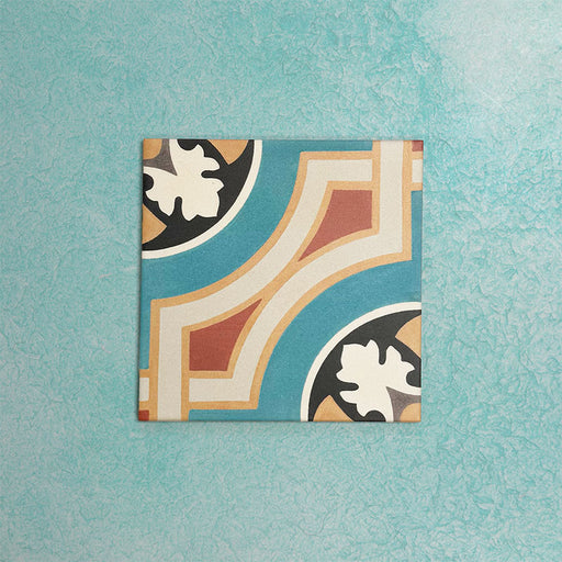 Baldosa Europa Helsinki 20 × 20 cm de estilo Victoriano Marroquí mostrada individualmente sobre un fondo aqua texturizado, con un patrón geométrico decorativo de esquina en tonos verde azulado, terracota, crema y negro en una imagen de producto en primer plano.