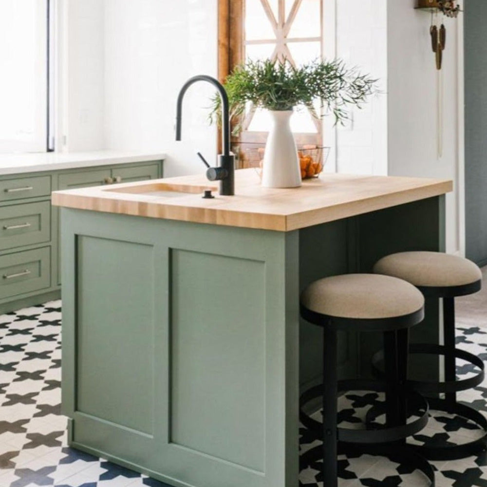 Interior de cocina con azulejos cerámicos de estilo marroquí Alhambra Compass 20x20 cm para suelo, mostrando un audaz patrón geométrico en blanco y negro, combinados con mobiliario en verde salvia y una isla de madera.