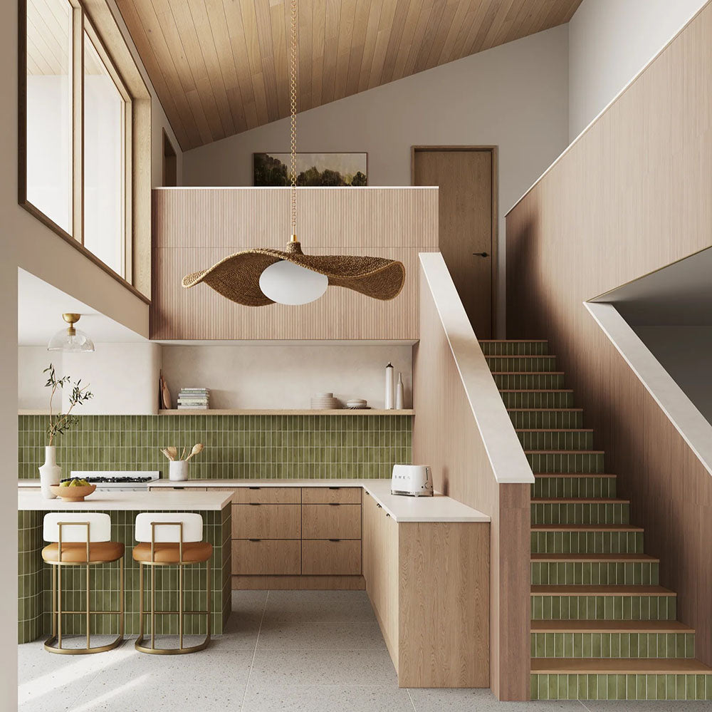 Cocina con azulejos de pared Atlas Green Mini Brick 5x15 cm en acabado mate, utilizados como salpicadero de cocina y en las contrahuellas de la escalera, mostrando tonos verdes intensos con un sutil efecto artesanal, combinados con mobiliario de madera cálida y suelo efecto terrazo.