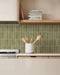 Cocina con azulejos de pared Atlas Green Mini Brick 5x15 cm en acabado mate, utilizados como salpicadero de cocina y en las contrahuellas de la escalera, mostrando tonos verdes intensos con un sutil efecto artesanal, combinados con mobiliario de madera cálida y suelo efecto terrazo.