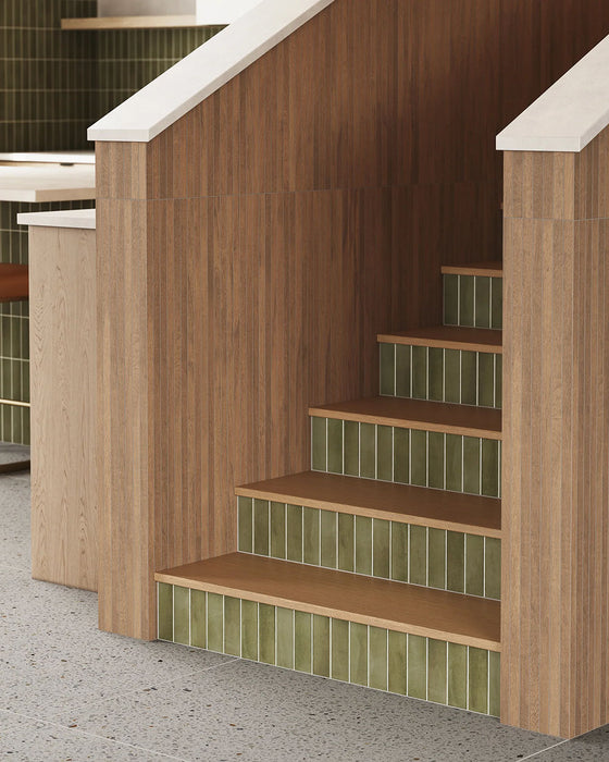 Cocina con azulejos de pared Atlas Green Mini Brick 5x15 cm en acabado mate, utilizados como salpicadero de cocina y en las contrahuellas de la escalera, mostrando tonos verdes intensos con un sutil efecto artesanal, combinados con mobiliario de madera cálida y suelo efecto terrazo.