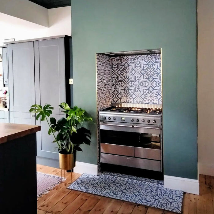 Interior de cocina con baldosas Europa Trondheim Blue 20 × 20 cm de estilo Victoriano Marroquí en tonos azul y blanco, instaladas como salpicadero decorativo y zona de hogar detrás de una cocina tipo range cooker de acero inoxidable.