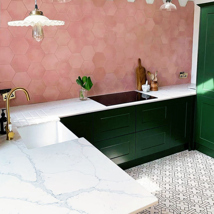 Azulejos de estilo marroquí Alhambra Palacio 20x20 cm en una cocina moderna con mobiliario en verde oscuro, encimeras efecto mármol y azulejos hexagonales rosados en la pared, creando un contraste elegante con el suelo geométrico decorativo.