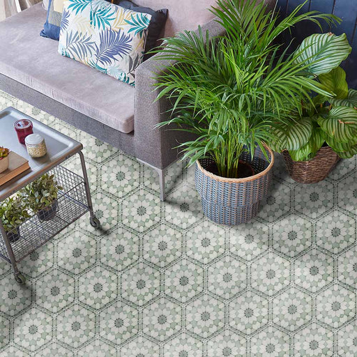 Baldosas hexagonales Maroush Verde 18,7x21,6 cm de estilo marroquí utilizadas en un salón, con patrón floral geométrico en verde suave y blanco, combinadas con sofá gris y plantas en maceta para un ambiente fresco y elegante.