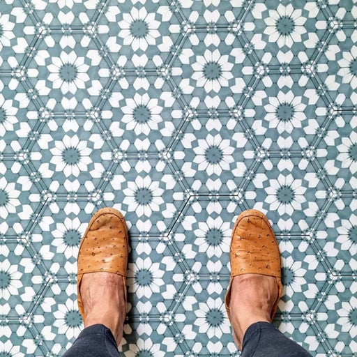 Vista superior de baldosas porcelánicas Maroush Azul Arcilla 18,7x21,6 cm en formato hexagonal de estilo marroquí para suelo, con patrón geométrico en azul y blanco, combinadas con zapatos en tono cuero para aportar escala y destacar el diseño decorativo.