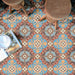 Vista cenital de baldosas de suelo Europa Hanover 20 × 20 cm de estilo Victoriano Marroquí en tonos azul, terracota y crema, formando un intrincado patrón decorativo, combinadas con taburetes de madera y una bandeja con revistas y vajilla.