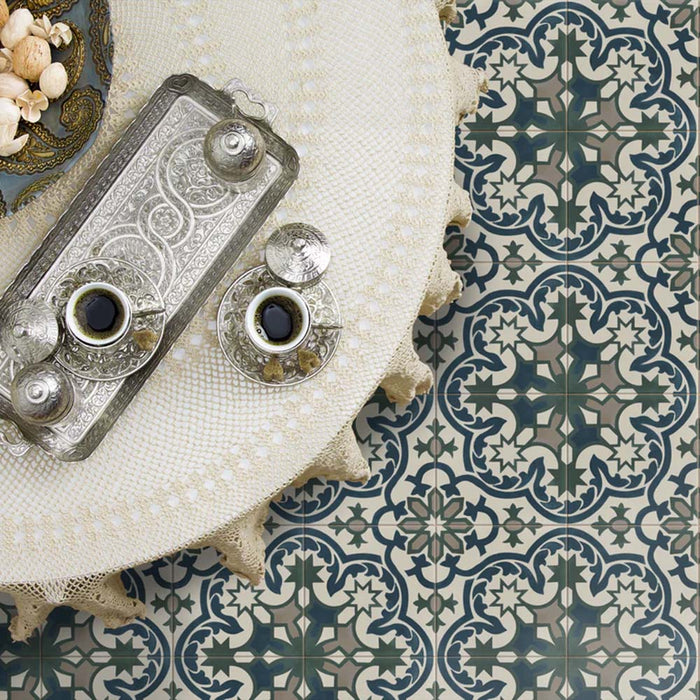 Escena de mesa colocada sobre baldosas Europa Prague 20 × 20 cm de estilo Victoriano Marroquí en tonos azul y verde salvia, con una bandeja decorativa plateada con tazas de café, situada junto a un mantel texturizado en una composición flat-lay de estilo lifestyle.