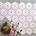 Baldosas hexagonales Maroush Rosa Empolvado 18,7x21,6 cm de estilo marroquí en composición flat lay, mostrando el detallado patrón floral geométrico en rosa y blanco junto a elementos decorativos y flores.