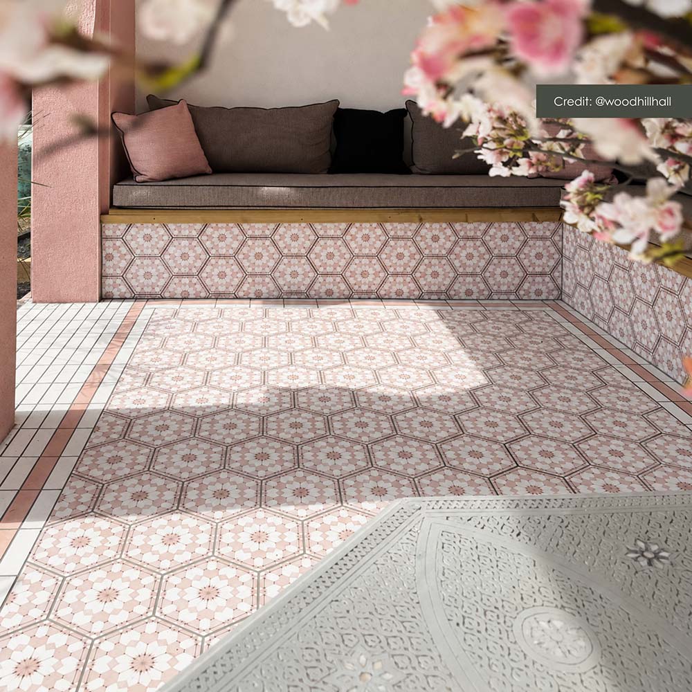Zona de estar exterior con azulejos hexagonales Maroush Dusty Pink de 18,7 × 21,6 cm de estilo marroquí, instalados tanto en el suelo como en los asientos de obra, con un elaborado patrón geométrico en rosa y blanco y azulejos de borde a juego.