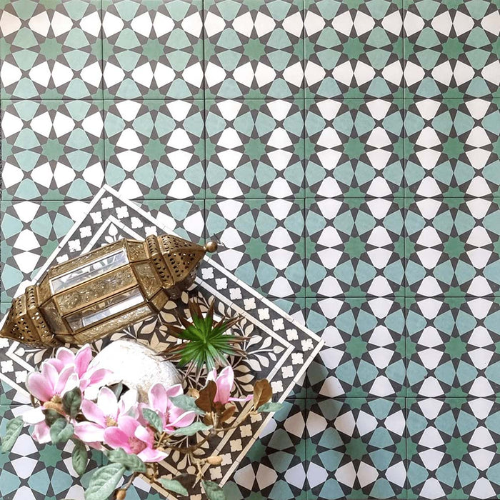 Interior de inspiración marroquí con azulejos decorativos Agraba Verde 20x20 cm en tonos verde, turquesa y blanco con motivos geométricos de estrellas, combinados con farol de latón, decoración floral y mesa auxiliar con diseño elaborado para un estilo artesanal auténtico.