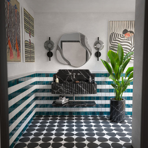 Baño ecléctico con azulejos decorados Pebble Beach Reversed Black de 20 × 20 cm en el suelo, combinados con azulejos de pared a rayas azules y blancas, un lavabo efecto mármol negro y llamativas obras de arte contemporáneo.