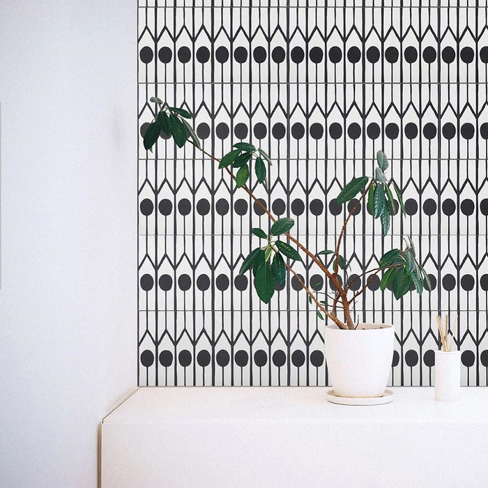 Azulejos de estilo marroquí Alhambra Felisa 20x20 cm utilizados como pared protagonista, mostrando un llamativo patrón lineal en blanco y negro con motivos circulares, combinados con una planta verde en maceta para un estilo minimalista contemporáneo.