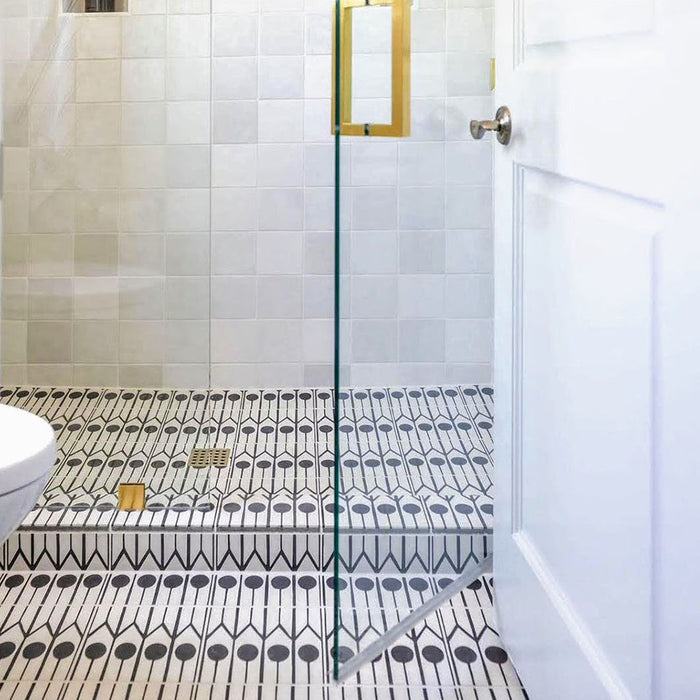 Azulejos de estilo marroquí Alhambra Felisa 20x20 cm colocados como suelo de baño, destacando un audaz patrón en blanco y negro junto a mobiliario en madera clara, grifería dorada y encimeras blancas para una estética moderna de inspiración marroquí.