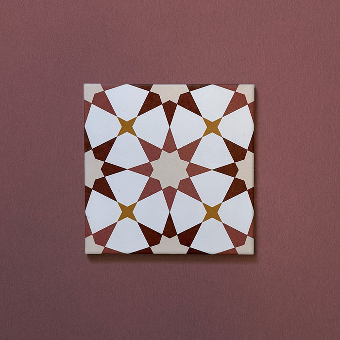 Primer plano del azulejo cerámico de estilo marroquí Agraba Cotto 20x20 cm, con patrón geométrico de estrellas en tonos terracota cálido, beige, mostaza y blanco sobre fondo burdeos suave.