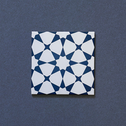 Primer plano del azulejo cerámico de estilo marroquí Agraba Azul Marino 20x20 cm, con un llamativo patrón geométrico de estrellas en azul marino intenso y blanco sobre fondo oscuro texturizado.