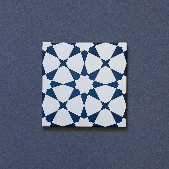 Primer plano del azulejo cerámico de estilo marroquí Agraba Azul Marino 20x20 cm, con un llamativo patrón geométrico de estrellas en azul marino intenso y blanco sobre fondo oscuro texturizado.