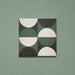 Single tile image showing the Geometry Circulo 20x20cm geometric patterned tile with green, black, and cream semicircle motifs, photographed against a soft green textured background.
