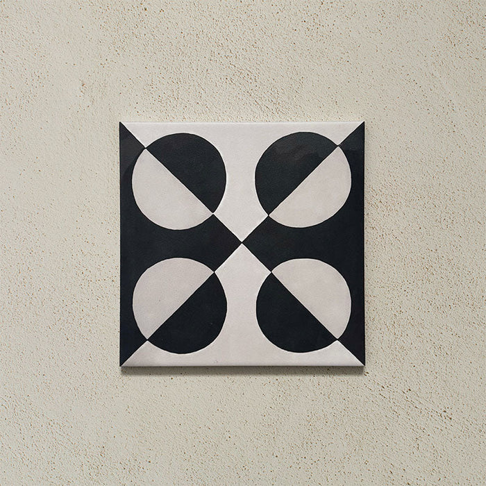 Single tile image showing the Geometry Illusion Noir 20x20cm geometric patterned tile with black and cream semicircles arranged in a bold symmetrical motif, photographed against a textured neutral background.