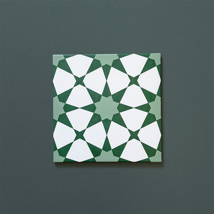 Primer plano del azulejo cerámico de estilo marroquí Agraba Verde 20x20 cm, con patrón geométrico de estrellas en tonos verde intenso y verde suave con detalles en blanco definido sobre fondo verde oscuro.