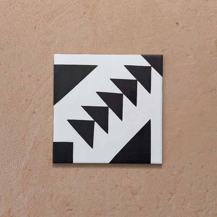 Azulejo individual de estilo marroquí Alhambra Alkazar 20x20 cm con patrón geométrico triangular en blanco y negro sobre superficie mate, ideal para suelos protagonistas e interiores contemporáneos.
