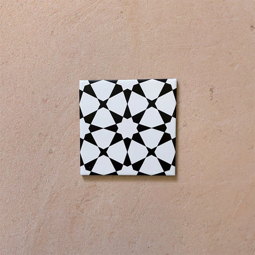 Primer plano del azulejo cerámico de estilo marroquí Agraba Mini Blanco y Negro 15x15 cm, con un llamativo patrón geométrico de estrellas en blanco y negro sobre fondo neutro.