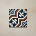 Single Brompton Grand 20x20cm Victorian-Moroccan-style ceramic tile featuring an intricate geometric and floral pattern in navy blue, terracotta, cream, and white tones, shown against a light beige background in a close-up view.