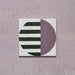 Single tile image showing the Geometry Seritina 20x20cm patterned tile with green horizontal stripes and a mauve semicircle on a cream base, photographed against a textured pink background.