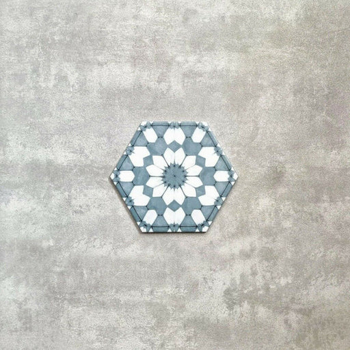 Baldosa porcelánica Maroush Azul Arcilla 18,7x21,6 cm en formato hexagonal de estilo marroquí con patrón floral geométrico en azul suave y blanco, ideal como revestimiento de pared para baño, salpicadero de cocina o suelos decorativos.