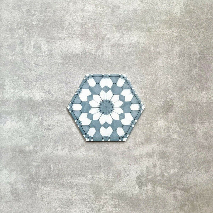Baldosa porcelánica Maroush Azul Arcilla 18,7x21,6 cm en formato hexagonal de estilo marroquí con patrón floral geométrico en azul suave y blanco, ideal como revestimiento de pared para baño, salpicadero de cocina o suelos decorativos.