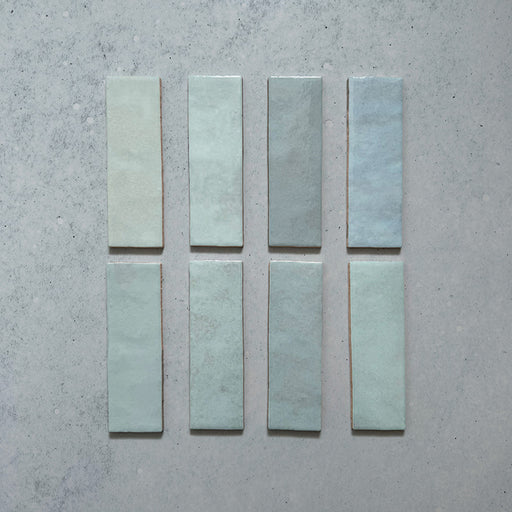 Vista cenital de azulejos de pared cerámicos Zellij Aqua Ladrillo 6,5 × 20 cm de estilo marroquí, presentados como piezas individuales, mostrando la suave variación tonal azul verdosa, el acabado brillante artesanal y los bordes ligeramente irregulares para un aspecto auténtico y lleno de carácter.