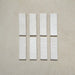 Vista cenital de azulejos de pared cerámicos Zellij Blanco Ladrillo 6,5 × 20 cm de estilo marroquí en color blanco, presentados como piezas individuales con sutil variación tonal y acabado artesanal sobre un fondo neutro texturizado.