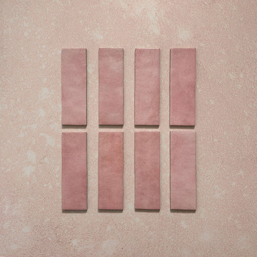 Vista cenital de azulejos de pared cerámicos Zellij Rosa Ladrillo 6,5 × 20 cm de estilo marroquí, presentados como piezas individuales, destacando la variación tonal suave, los bordes ligeramente irregulares y el acabado brillante artesanal en tonos rosados sobre un fondo texturizado.