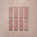 Vista cenital de azulejos de pared cerámicos Zellij Rosa Ladrillo 6,5 × 20 cm de estilo marroquí, presentados como piezas individuales, destacando la variación tonal suave, los bordes ligeramente irregulares y el acabado brillante artesanal en tonos rosados sobre un fondo texturizado.
