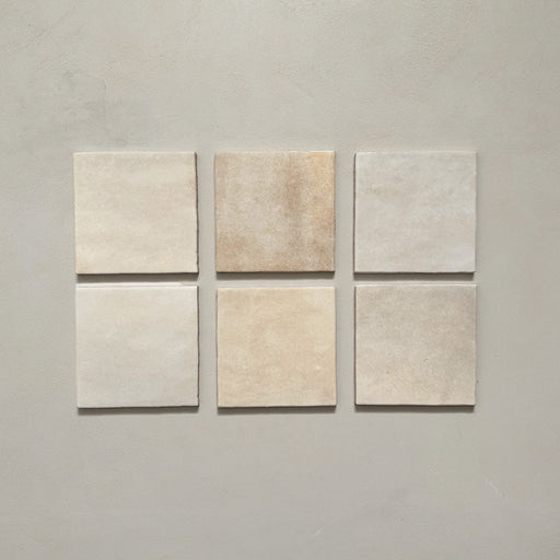 Vista cenital de azulejos de pared cerámicos Zellij Ocre Cuadrado 13,2 × 13,2 cm de estilo marroquí, presentados como piezas individuales, destacando la variación tonal suave, los bordes ligeramente irregulares y el acabado brillante artesanal en tonos neutros cálidos sobre un fondo liso.